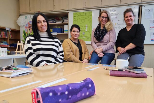 Vier Frauen sitzen hinter einem Tisch mit Federmäppchen und Schulmaterialien