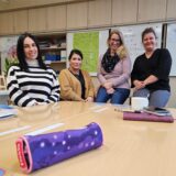 Vier Frauen sitzen hinter einem Tisch mit Federmäppchen und Schulmaterialien
