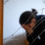Eine Frau vergräbt ihr Gesicht in ihren Händen. Sie sitzt hinter einer zerstörten Glasscheibe.