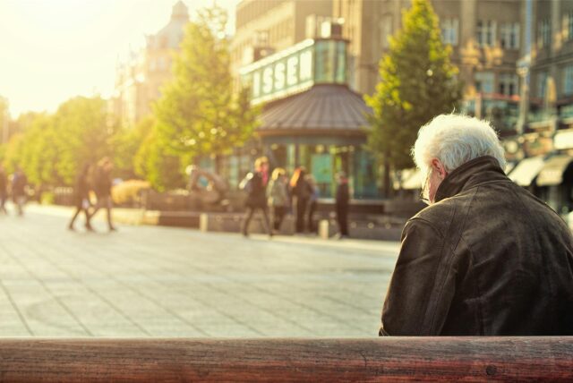 Eine alte Person sitzt allein auf einer Bank.