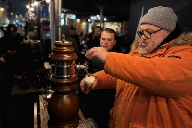Christian Wolf zapft in oranger Jacke ein Bier.