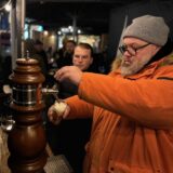 Christian Wolf zapft in oranger Jacke ein Bier.