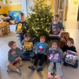 Sieben Kinder stehen und sitzen vor einem Weihnachtsbaum und halten Bücher in der Hand.