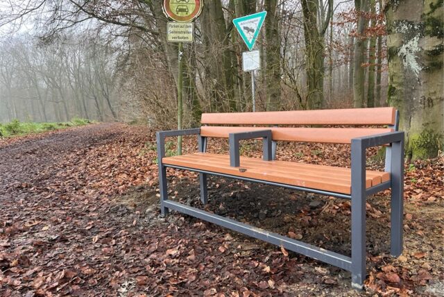 Eine Bank steht am Eingang zum Telgenbusch, in der Mitte der Sitzfläche ist eine Eisenstange montiert.