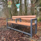 Eine Bank steht am Eingang zum Telgenbusch, in der Mitte der Sitzfläche ist eine Eisenstange montiert.