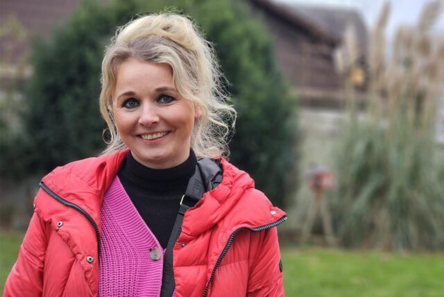 Isabel Auffenberg steht offenbar auf einer Rasenfläche. Sie trägt eine rote Jacke und lächelt in die Kamera.