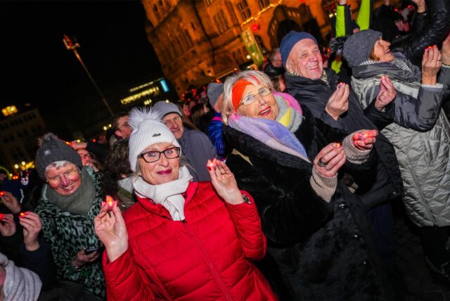 Menschen in Winterkleidung stehen am 13. Dezember 2024 auf dem Rathausplatz Recklinghausen und halten für einen Weltrekord-Versuch LEDs in den Händen.