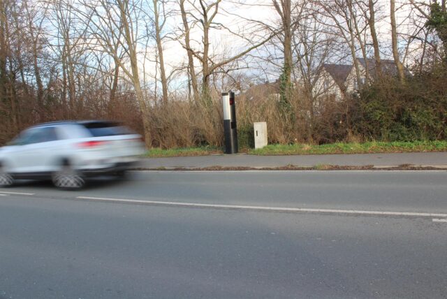 Eine Blitzersäule am Straßenrand, ein Auto fährt vorbei.
