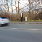 Eine Blitzersäule am Straßenrand, ein Auto fährt vorbei.