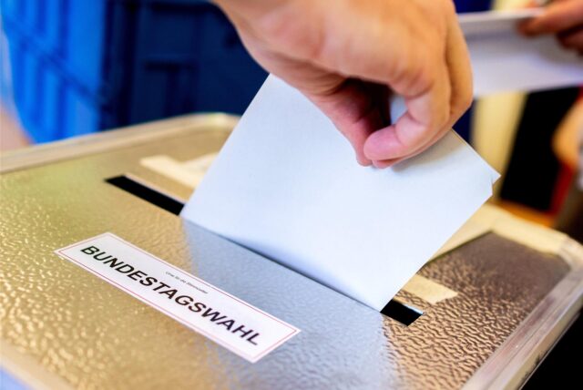 Eine Hand steckt einen Wahlzettel in eine Wahlurne
