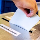 Eine Hand steckt einen Wahlzettel in eine Wahlurne