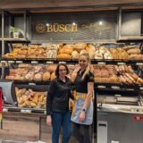 Verkäuferinnen der Bäckerei Büsch stehen in einer Filiale vor der Brot- und Brötchenauslage.