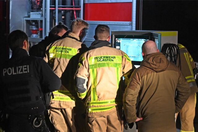 Einsatzkräfte von Polizei und Feuerwehr schauen sich die Aufnahmen einer Drohne auf einem Bildschirm an.