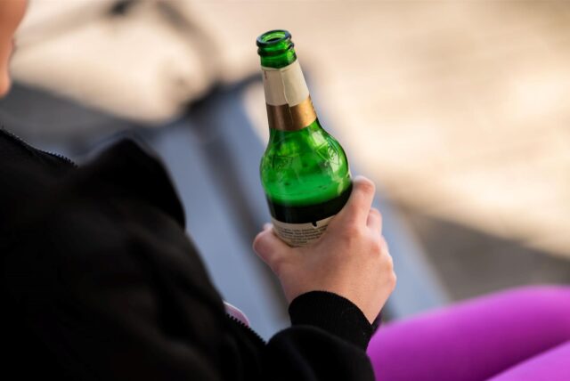 Eine Person hält eine halbvolle Flasche Bier in der Hand.
