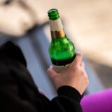 Eine Person hält eine halbvolle Flasche Bier in der Hand.