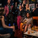 Vier Frauen und ein Mann in festlicher Kleidung und Partyhüten feiern Silvester.