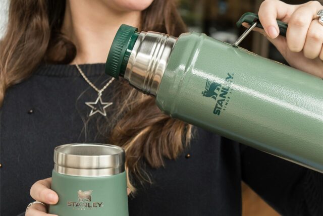Eine Frau hält eine Thermoskanne und einen Becher von Stanley in den Händen.