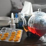 Medikamente und eine Kanne und Tasse Tee zur Bekämpfung einer Erkältung sind auf einem Nachttisch aufgestellt.