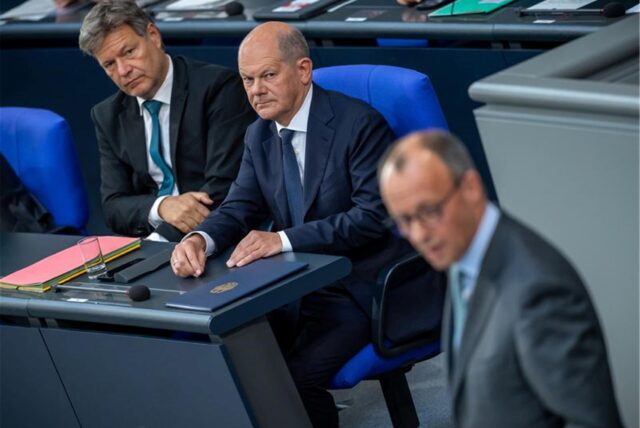 Bundeskanzler Olaf Scholz (SPD) sitzt neben Robert Habeck und schaut misstrauisch zu Friedrich Merz.