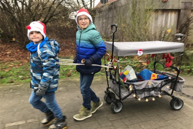 Bennet und Julius ziehen einen adventlich geschmückten Bollerwagen.