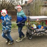 Bennet und Julius ziehen einen adventlich geschmückten Bollerwagen.