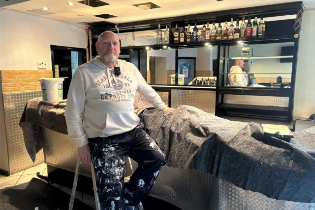 Ein Mann in Arbeiterhose sitzt in einer Bar in Waltrop auf einer Leiter. Seine Hand stützt er auf den Tresen