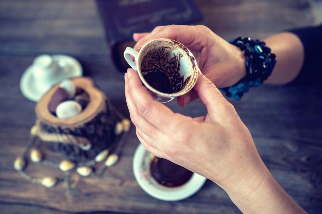 Eine Frau hält eine Kaffeetasse mit Kaffeesatz in beiden Händen, um den Kaffeesatz zu lesen.