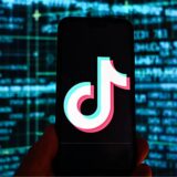 Das Logo der Video-App TikTok ist auf einem Smartphone vor einem Bildschirm mit Börsenkursen im Hintergrund zu sehen.