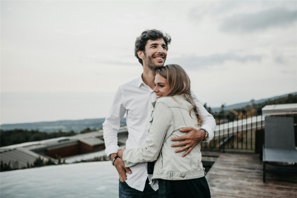 Ein Paar steht Arm in Arm auf einer Terrasse und lacht.