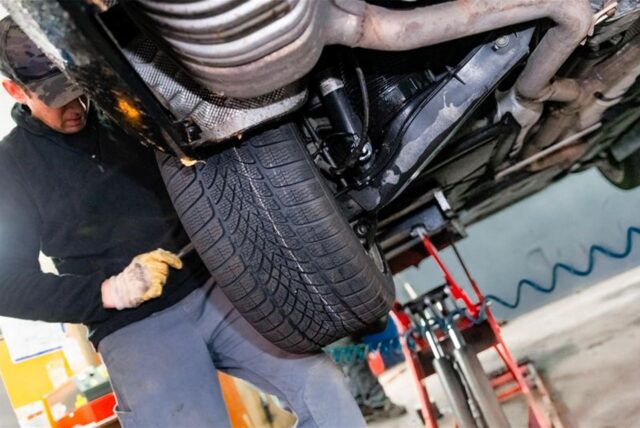 Ein Kfz-Mechatroniker montiert in einer Werkstatt Winterreifen an einem Auto.