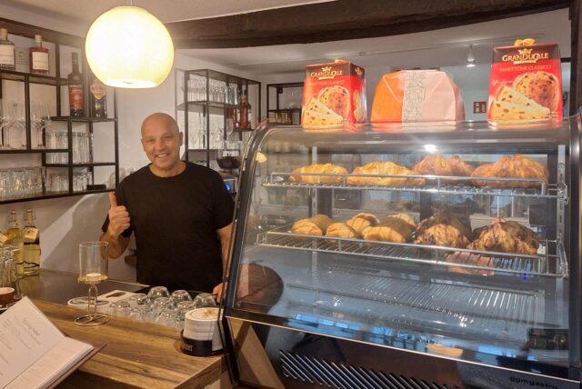 Ex-BVB-Spieler Guiseppe Reina steht hinter Theke in seinem neu eröffneten Austro-Italian Bistro auf der Massener Straße in Unna. Er trägt eine Glatze und ein schwarzes T-Shirt. Er streckt den Daumen nach oben. Rechts im Bild ist italienisches Gebäck zu sehen.