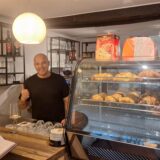 Ex-BVB-Spieler Guiseppe Reina steht hinter Theke in seinem neu eröffneten Austro-Italian Bistro auf der Massener Straße in Unna. Er trägt eine Glatze und ein schwarzes T-Shirt. Er streckt den Daumen nach oben. Rechts im Bild ist italienisches Gebäck zu sehen.