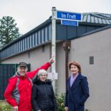 Drei Menschen enthüllen ein Straßenschild.