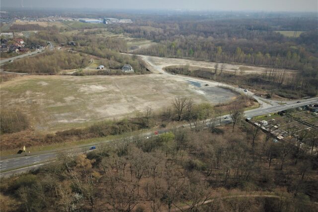 Auf dieser Fläche an der B235 in Habinghorst steht heute eine Groß-Notunterkunft für Geflüchtete des Landes NRW (links). Auf dem schmaleren Stück oberhalb des Baches im Hintergrund sollen ein Fußballplatz und eine Kita gebaut werden.