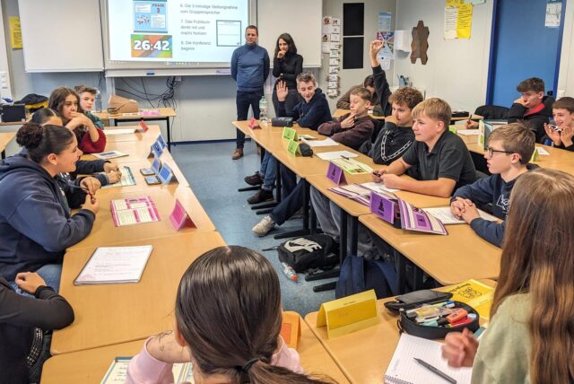Schüler und Schülerinnen der neunten Klasse der Gesamtschule sitzen sich an Tischen gegenüber und diskutieren über Cannabis.