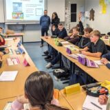 Schüler und Schülerinnen der neunten Klasse der Gesamtschule sitzen sich an Tischen gegenüber und diskutieren über Cannabis.