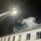 Eine ausgefahrene Drehleiter fährt an einen Dachstuhl heran, aus dem Rauch aufsteigt.