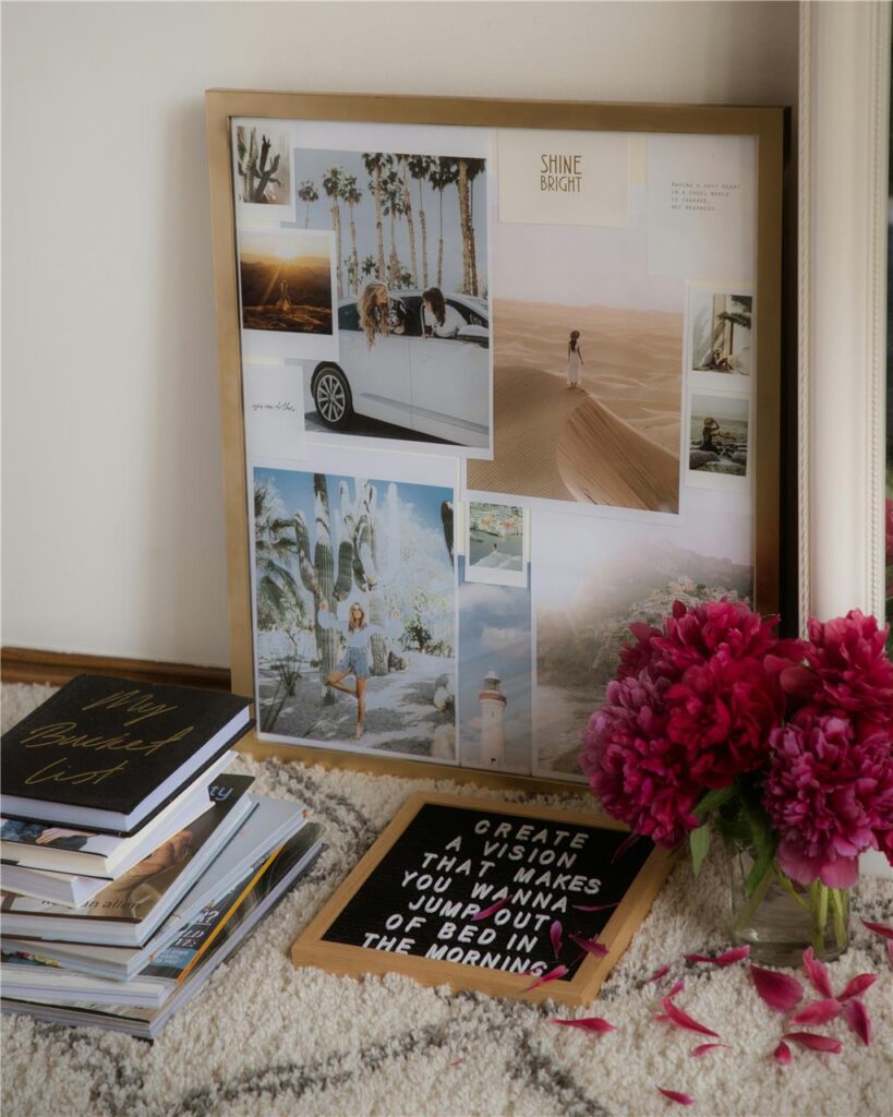 An einer Wand lehnt ein eingerahmtes Vision Board mit Bildern und Notizzetteln zum Thema Urlaub und Reisen. Auf dem Teppich auf dem Boden davor liegt ein Stapel Bücher und eine Tafel mit dem Spruch An einer Wand lehnt ein eingerahmtes Vision Board mit Bildern und Notizzetteln zum Thema Urlaub und Reisen. Auf dem Teppich auf dem Boden davor liegt ein Stapel Bücher und eine Tafel mit dem Spruch
