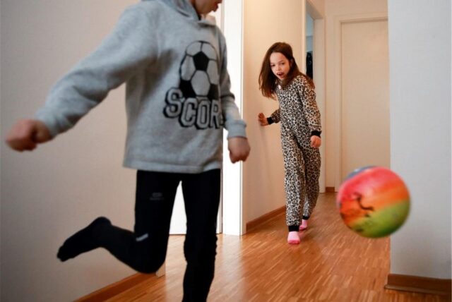 Zwei Kinder spielen in einer Wohnung mit einem Ball.