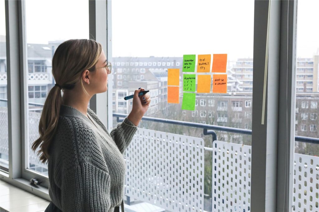 Eine Frau steht in ihrem Büro am Fenster und beschriftet Post-its, um ihre Strategie zu planen.
