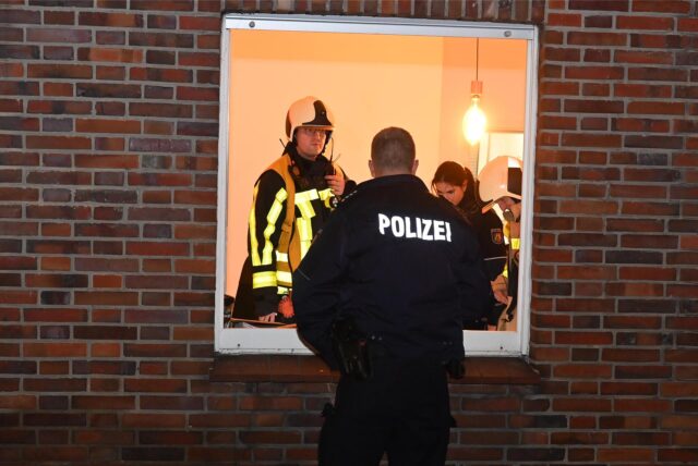 Ein Feuerwehrmann und ein Polizist stehen am Fenster der Brandwohnung in Dorsten.