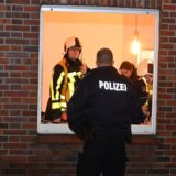 Ein Feuerwehrmann und ein Polizist stehen am Fenster der Brandwohnung in Dorsten.
