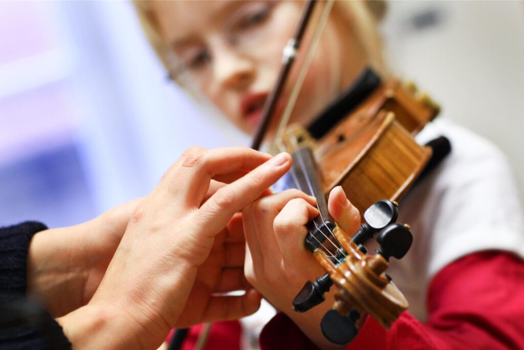 Eine Musiklehrerin korrigiert die Hand einer Schülerin beim Geigenspiel. Musikunterricht ist für die Persönlichkeitsbildung von Kindern zentral, trotzdem erhalten viele Pädagoginnen und Pädagogen nur Honorare.