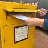 Ein Mann steckt einen Brief in einen gelben Briefkasten