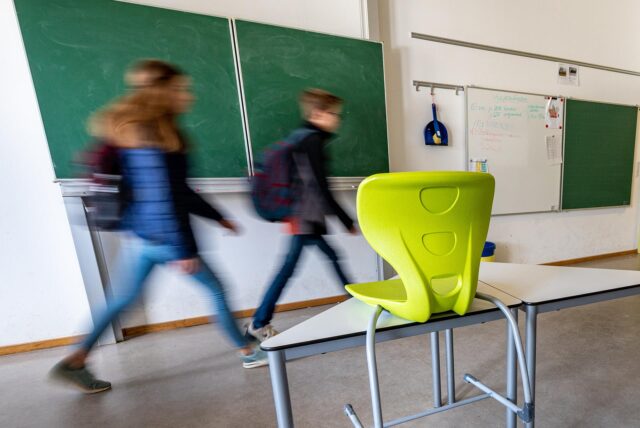 Schüler gehen nach Unterrichtsschluss aus einem leeren Klassenzimmer.