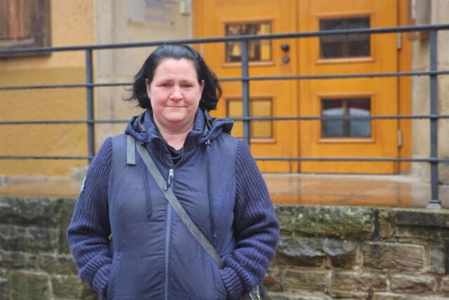 Frau steht vor einer Treppe, die zu der Tür eines Gebäudes führt.