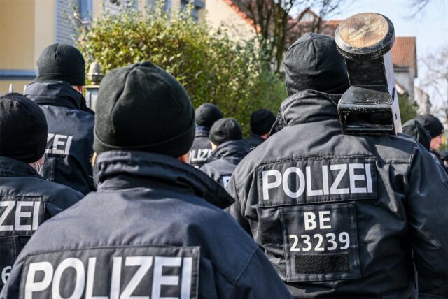 Beamte eines Spezialeinsatzkommandos sind von hinten zu sehen. Sie tragen Mützen. Einer hat eine Türramme geschultert.