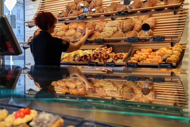 Eine Frau nimmt ein Brot aus einem Regal in einer Bäckerei.