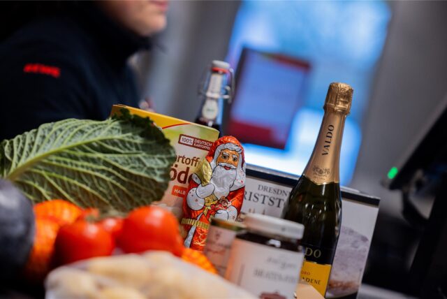 Verschiedene Waren eines Weihnachtseinkaufs liegen auf einem Kassenband an der Kasse in einem Supermarkt.