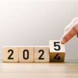 Eine Hand dreht einen von vier Würfeln um, sodass aus 2024 die Jahreszahl 2025 wird.